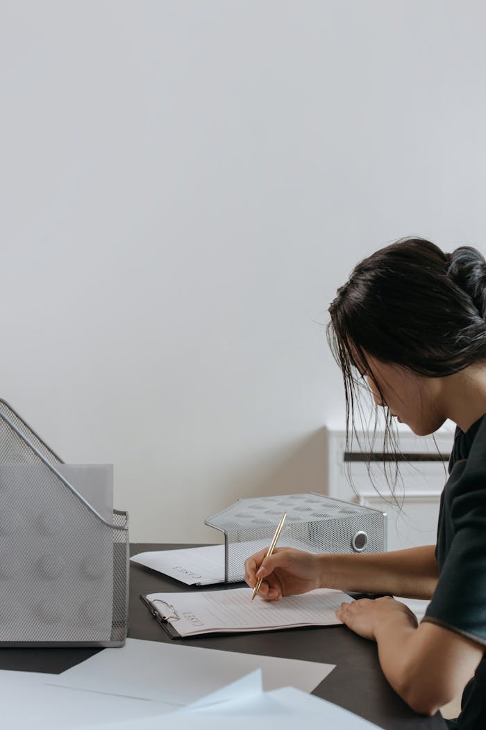 Asian woman writing notes in an office work environment, focusing on productivity